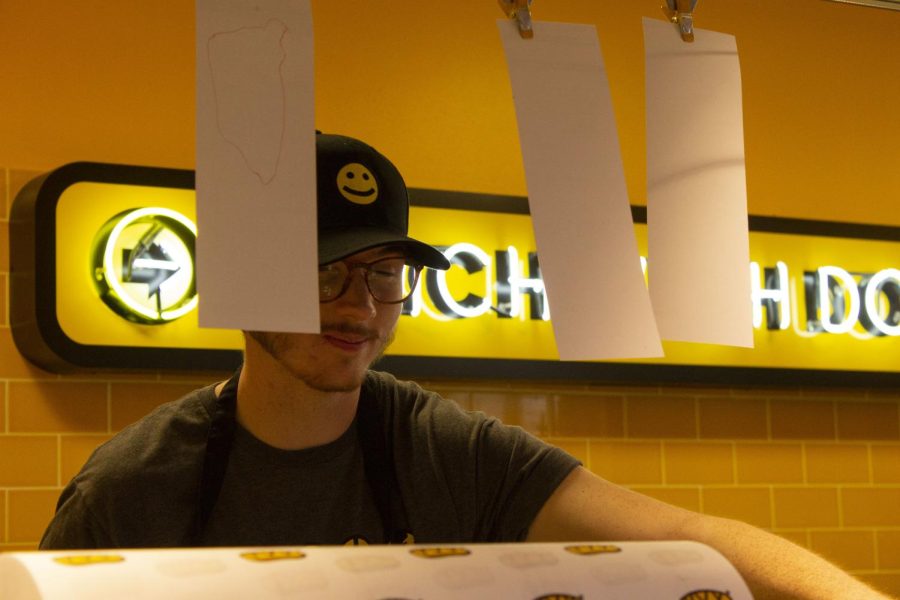 Aidan Driscoll with Which Wich Superior Sandwiches pulls a hot sandwich off a conveyor belt to wrap and give to students. Photo taken March 9, 2022. 