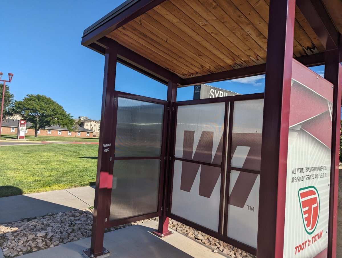 The bus stop outside of the Sybil B. Harrington Fine Arts Center. The bus station has the West Texas A&M University colors and logo. The stop sits empty, with no students visible.